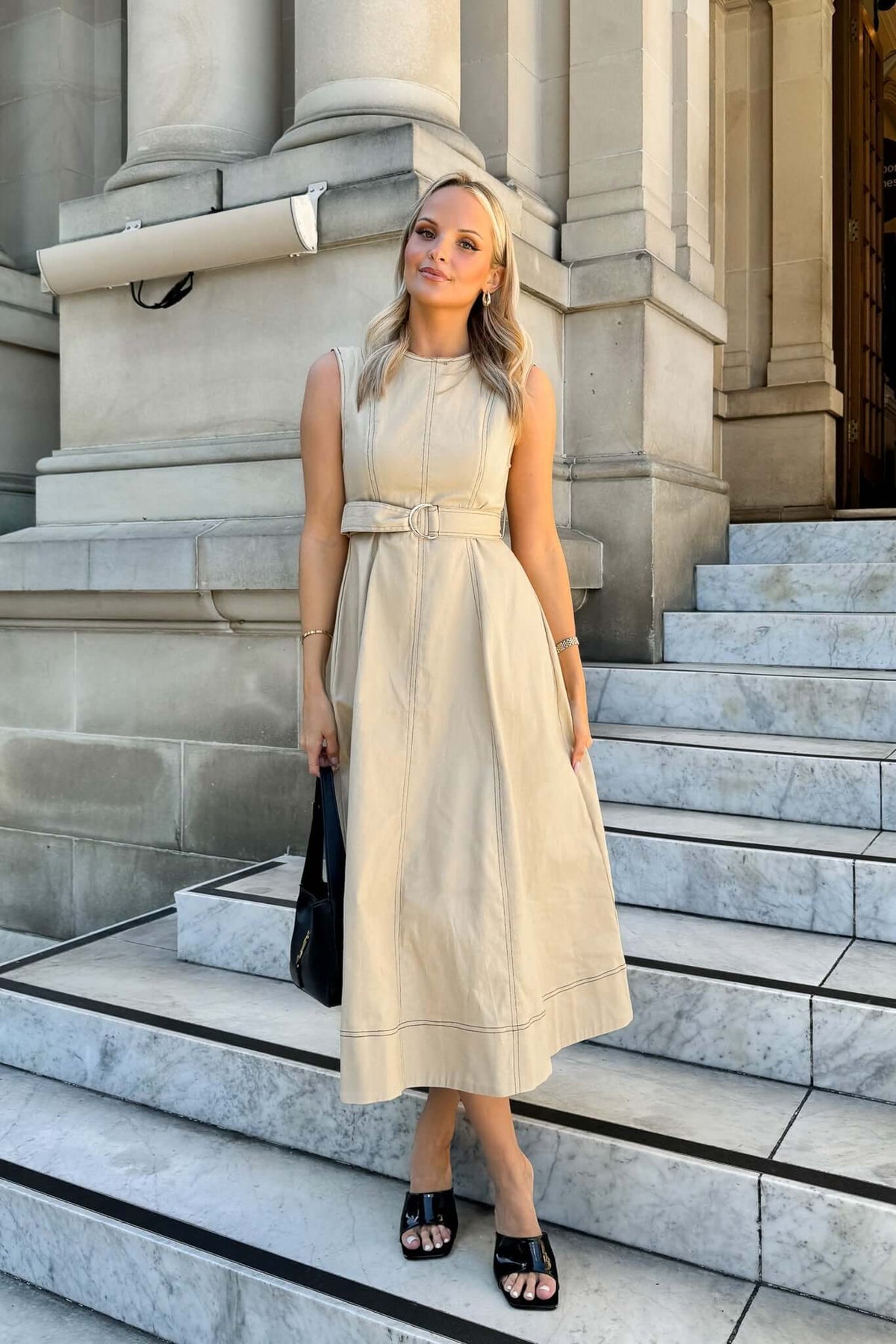Model wearing a beige denim midi dress with a removable belt, standing on marble steps.