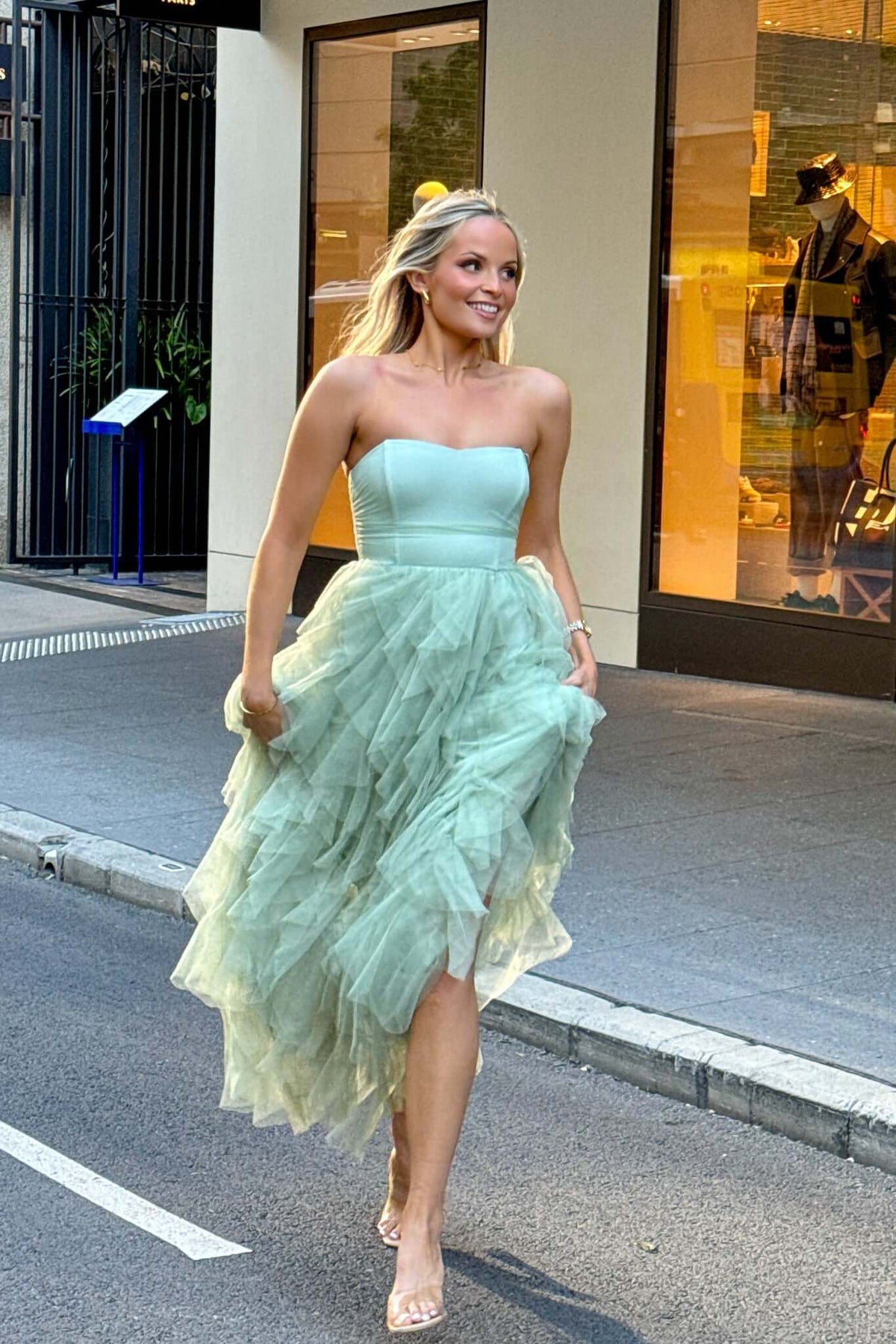 Model wearing a strapless Carrie Maxi Dress in mint green with a tulle overlay, walking stylishly down the street.