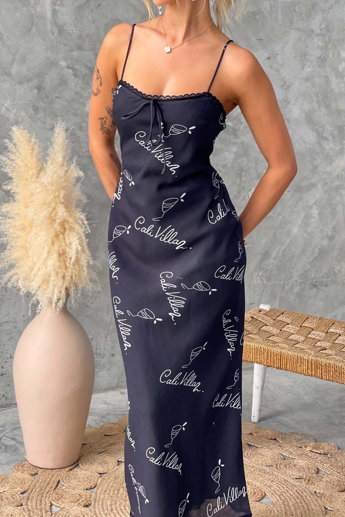 Model in a black Dolomite maxi dress with adjustable straps and tie detail, styled with natural decor.