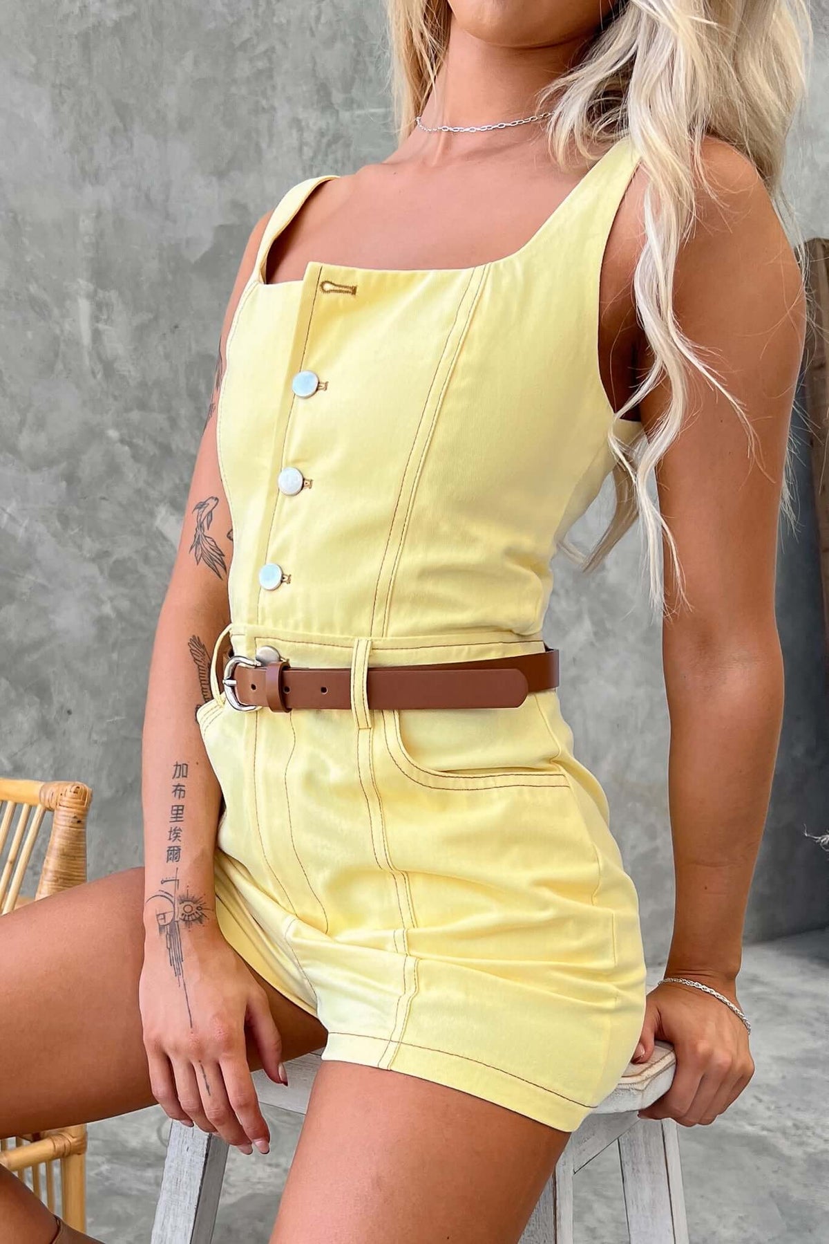 Yellow denim playsuit with button-up front and belt, styled with a relaxed fit against a neutral background.