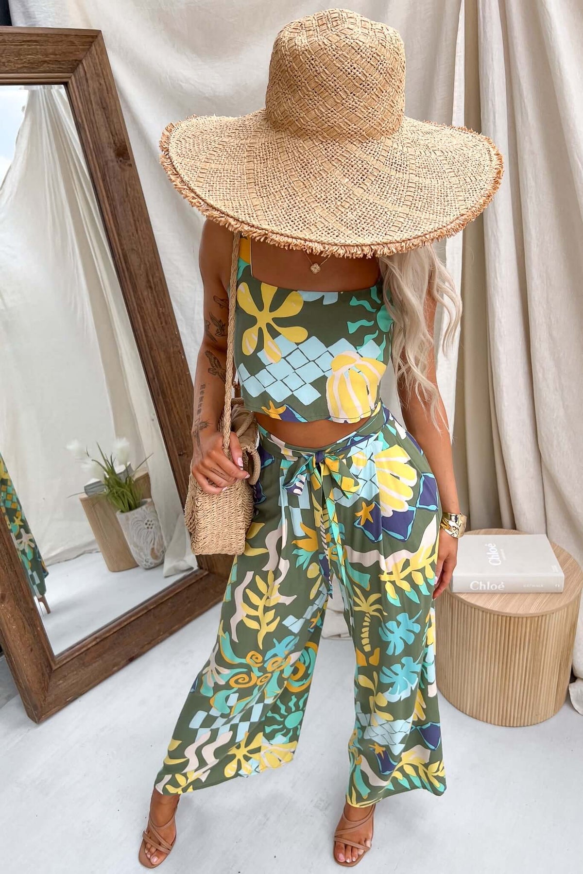 Model wearing floral Warana Pants with removable tie, paired with a patterned top and wide-brimmed hat.