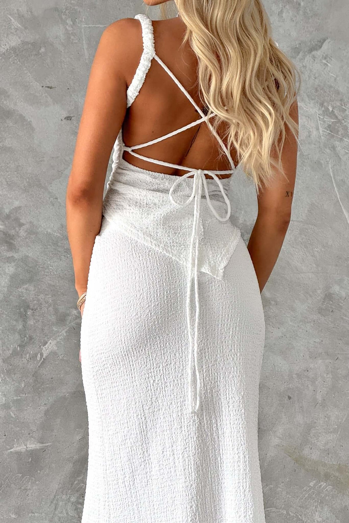Brigitte Top featuring a tie-back design, elastic straps, and textured fabric, showcasing an asymmetric hem.