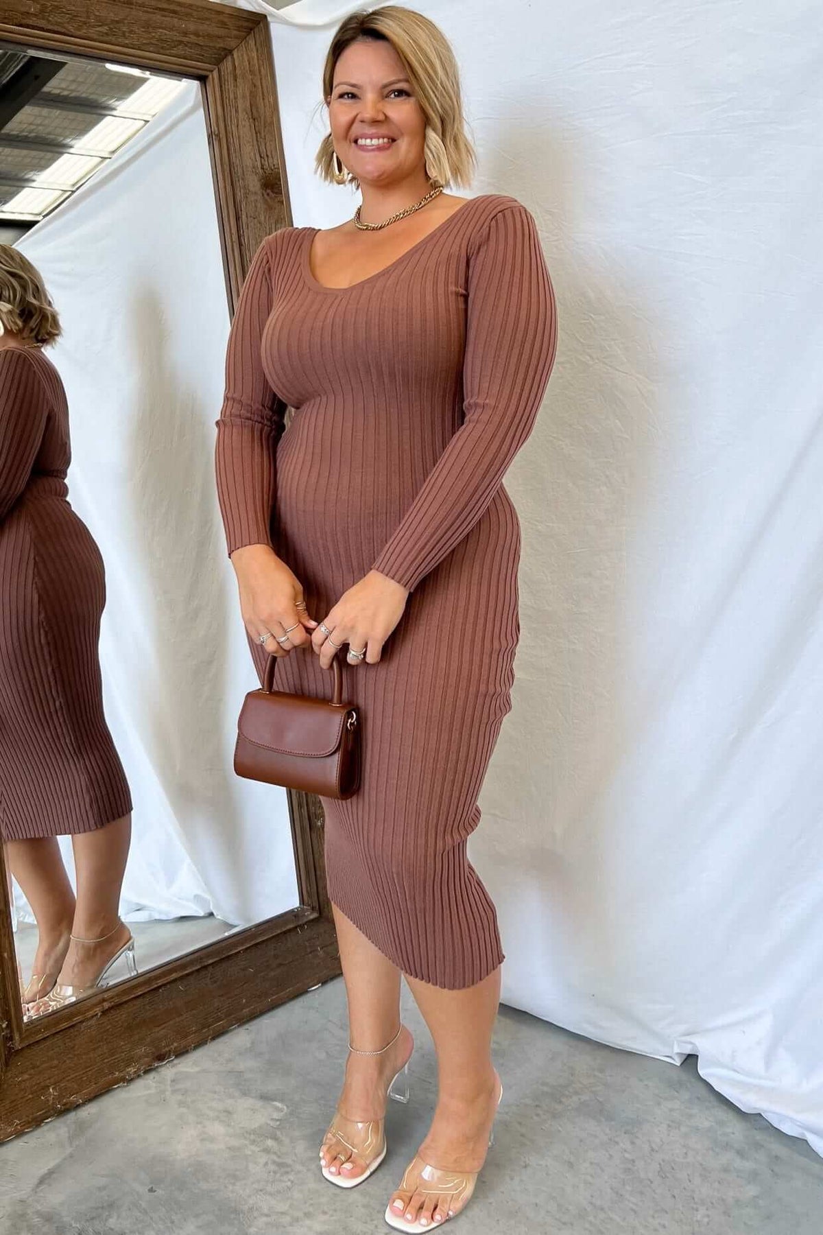 Aquino Midi Dress featuring a V-neckline and ribbed knit design, styled with a brown handbag and clear heels.
