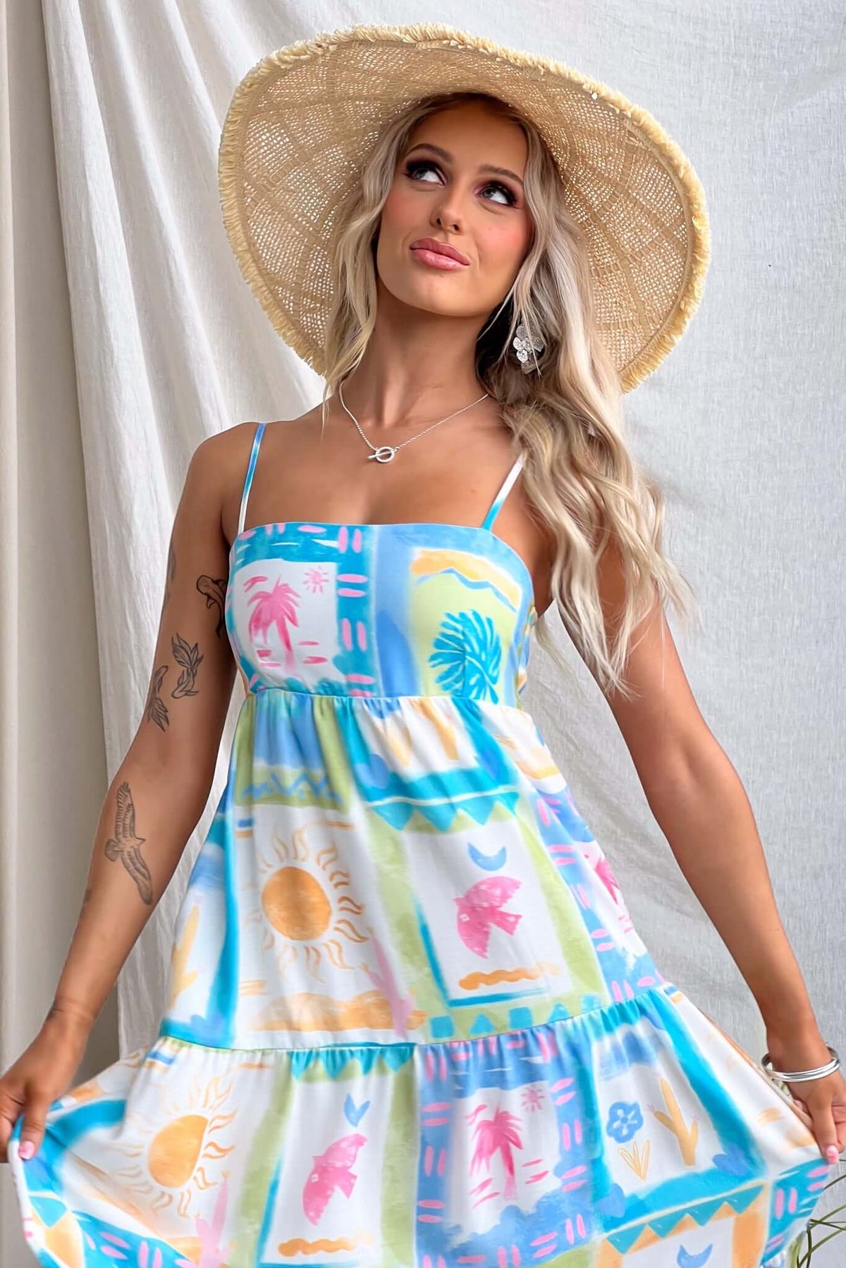 Model wearing a colorful, patterned Maxi Dress with adjustable straps and a wide-brimmed hat.