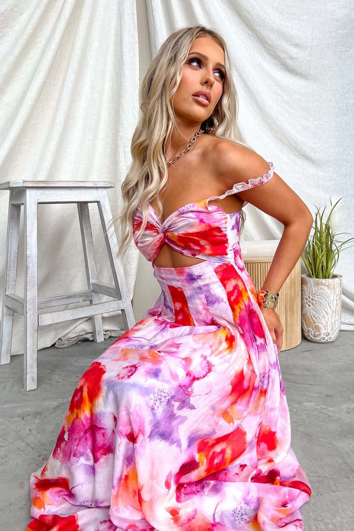 Model wearing Estelle Midi Dress with floral patterns, featuring cut-out waist and elastic straps, styled in a bright setting.