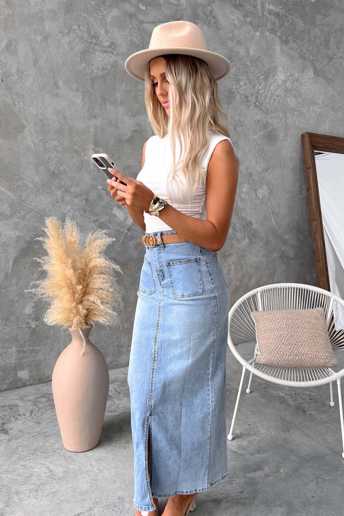 Model wearing Naomi Denim Maxi Skirt with a mid-high waist, front split, and pockets; styled with a hat and phone.