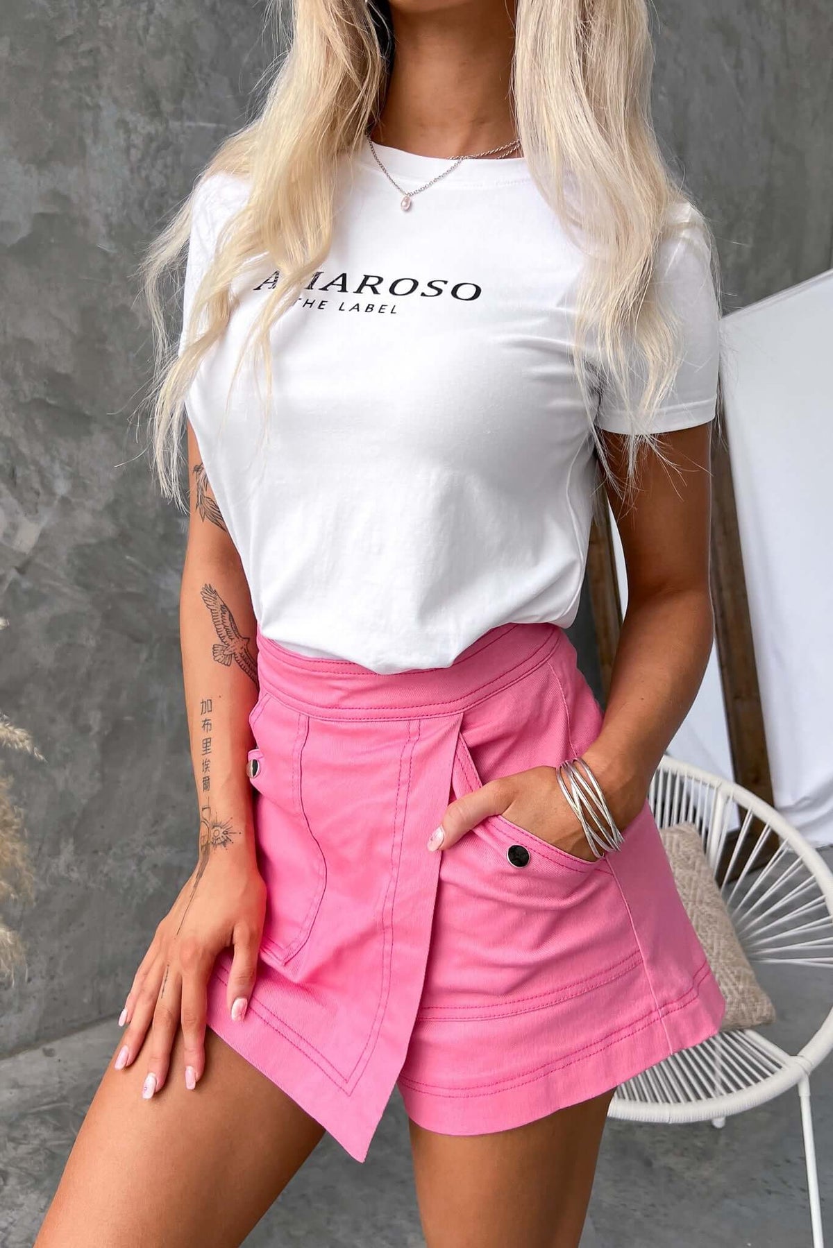 Woman wearing a white logo t-shirt with pink skort, showcasing a stylish and trendy summer outfit.
