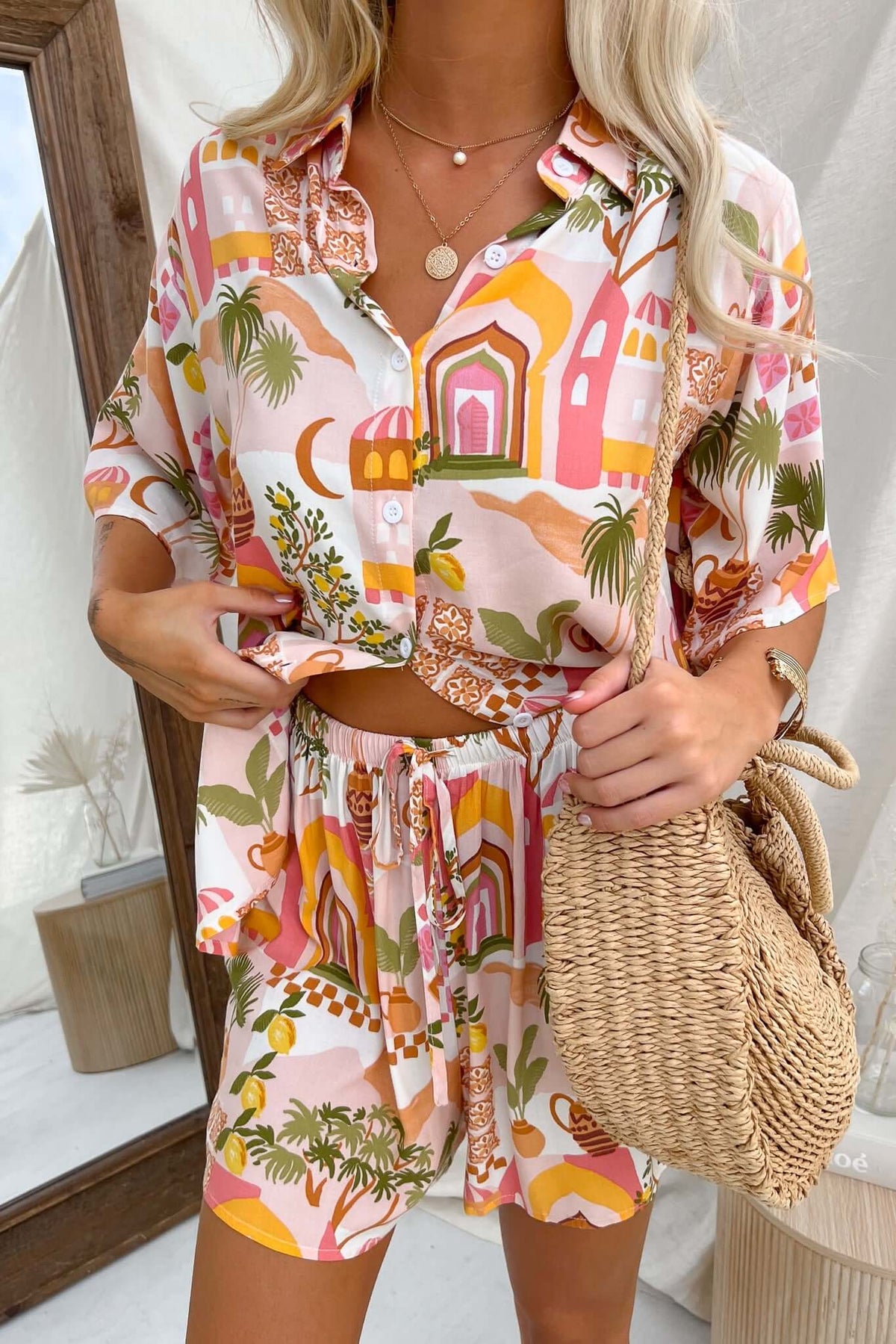 Model wearing the Junia Set featuring a colorful button-up shirt and mid-high waist shorts, styled with a woven bag.