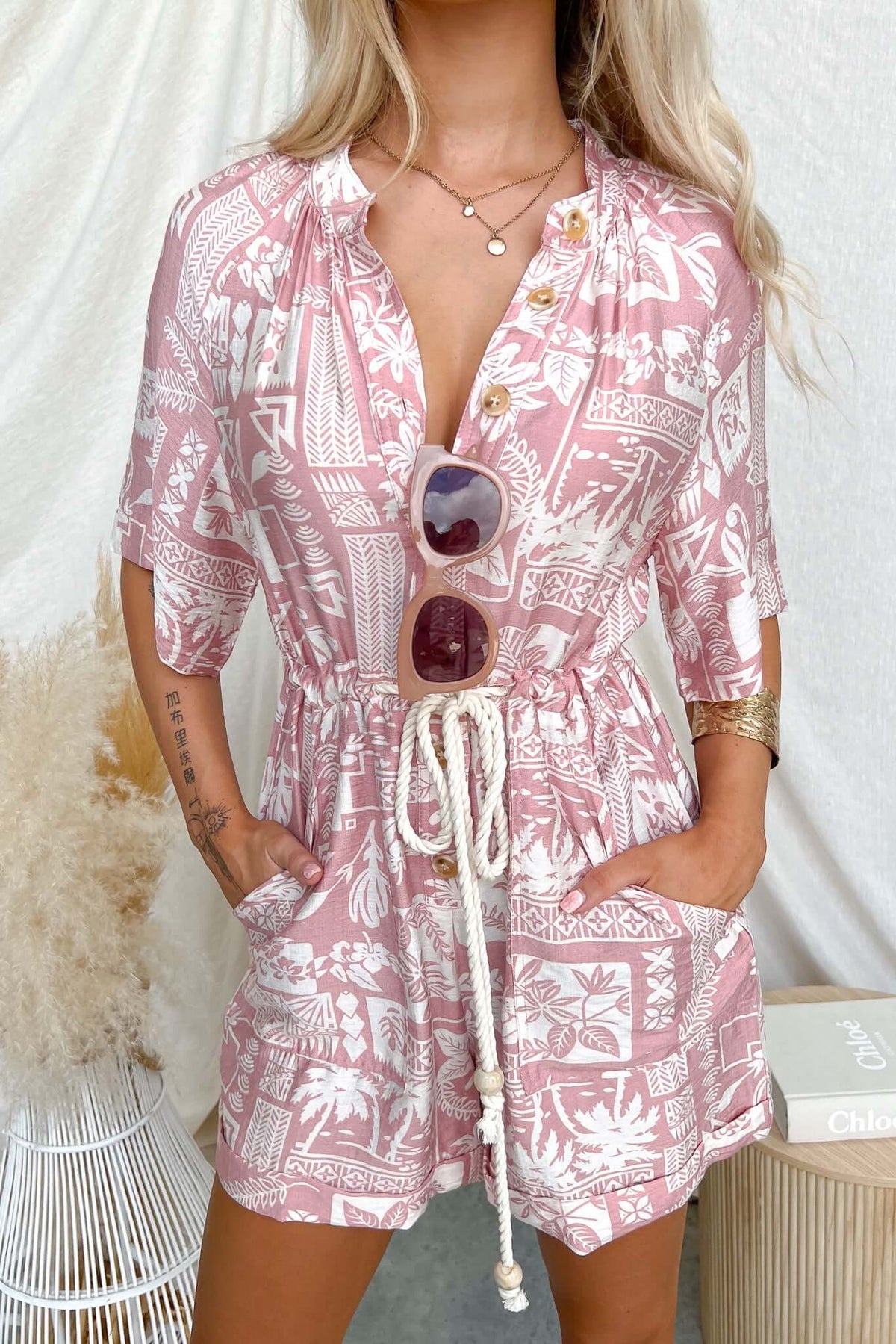 Model wearing Huxley Playsuit with button-up front, elastic waistband, and pockets, featuring a tropical print.