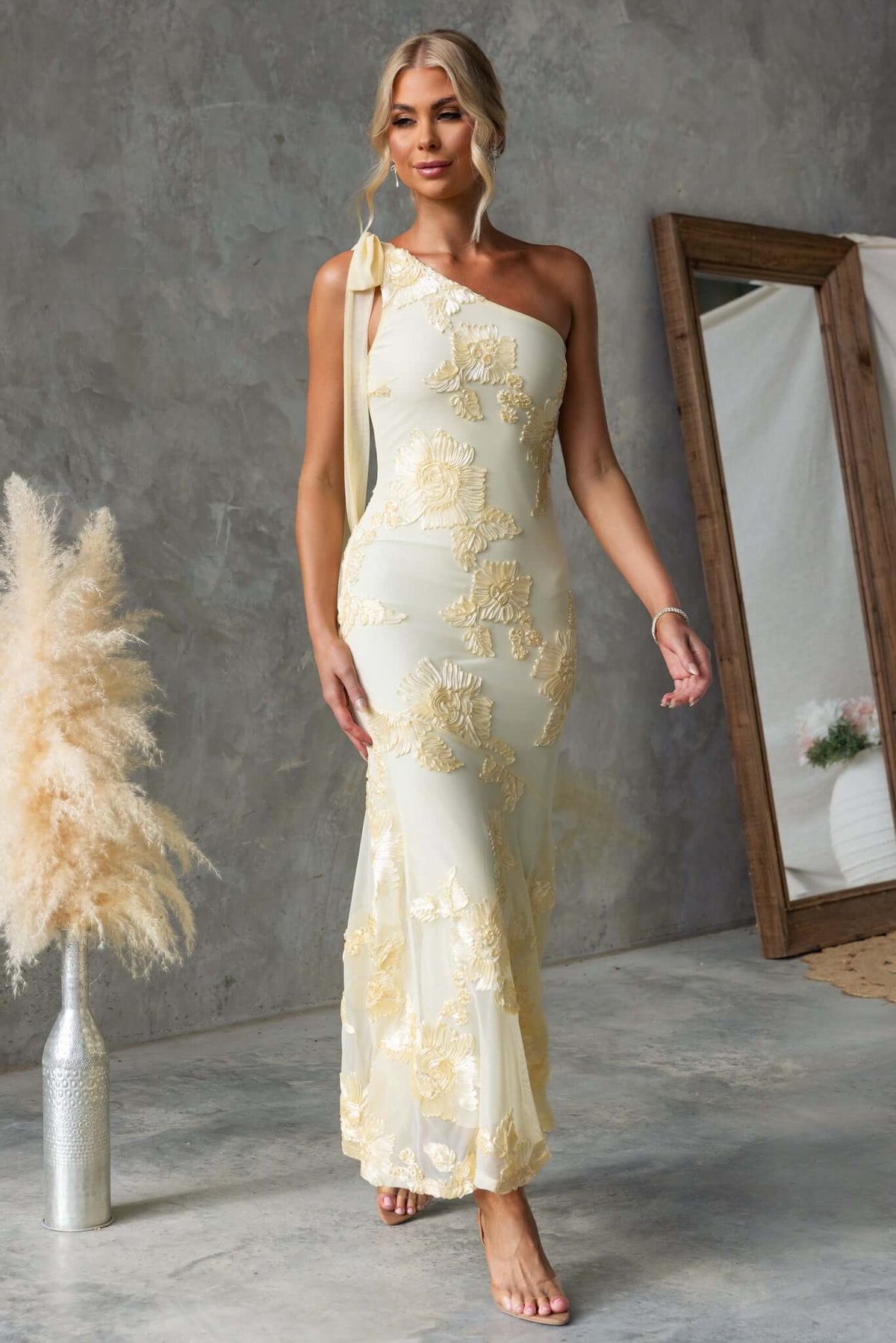 Woman wearing Inspire Maxi Dress with one-shoulder neckline, tie shoulder, and embroidered material.