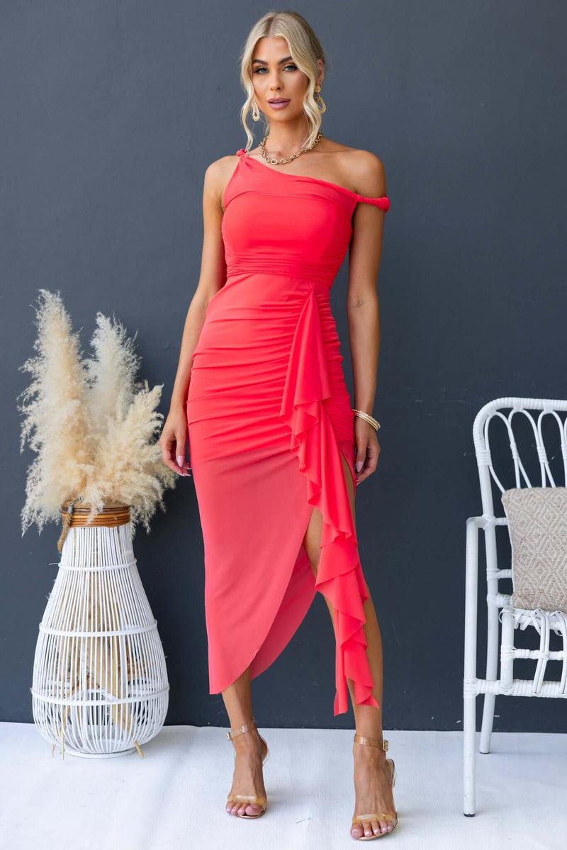 Model wearing a coral Iroha Maxi Dress with ruffle detail and asymmetric hem against a dark background.