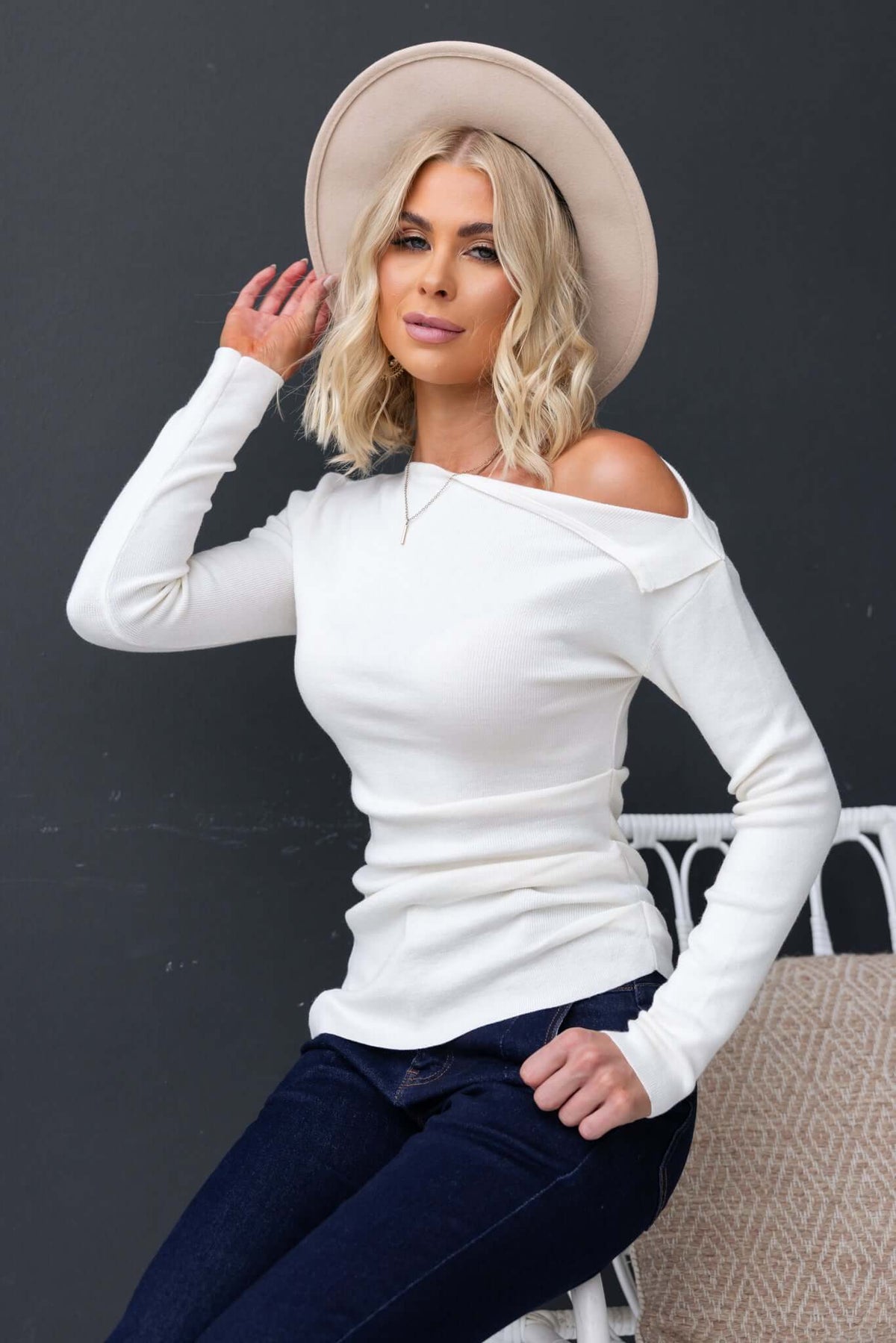 Model wearing Isla Top with asymmetric neckline and hem in white, styled with a hat and casual jeans.