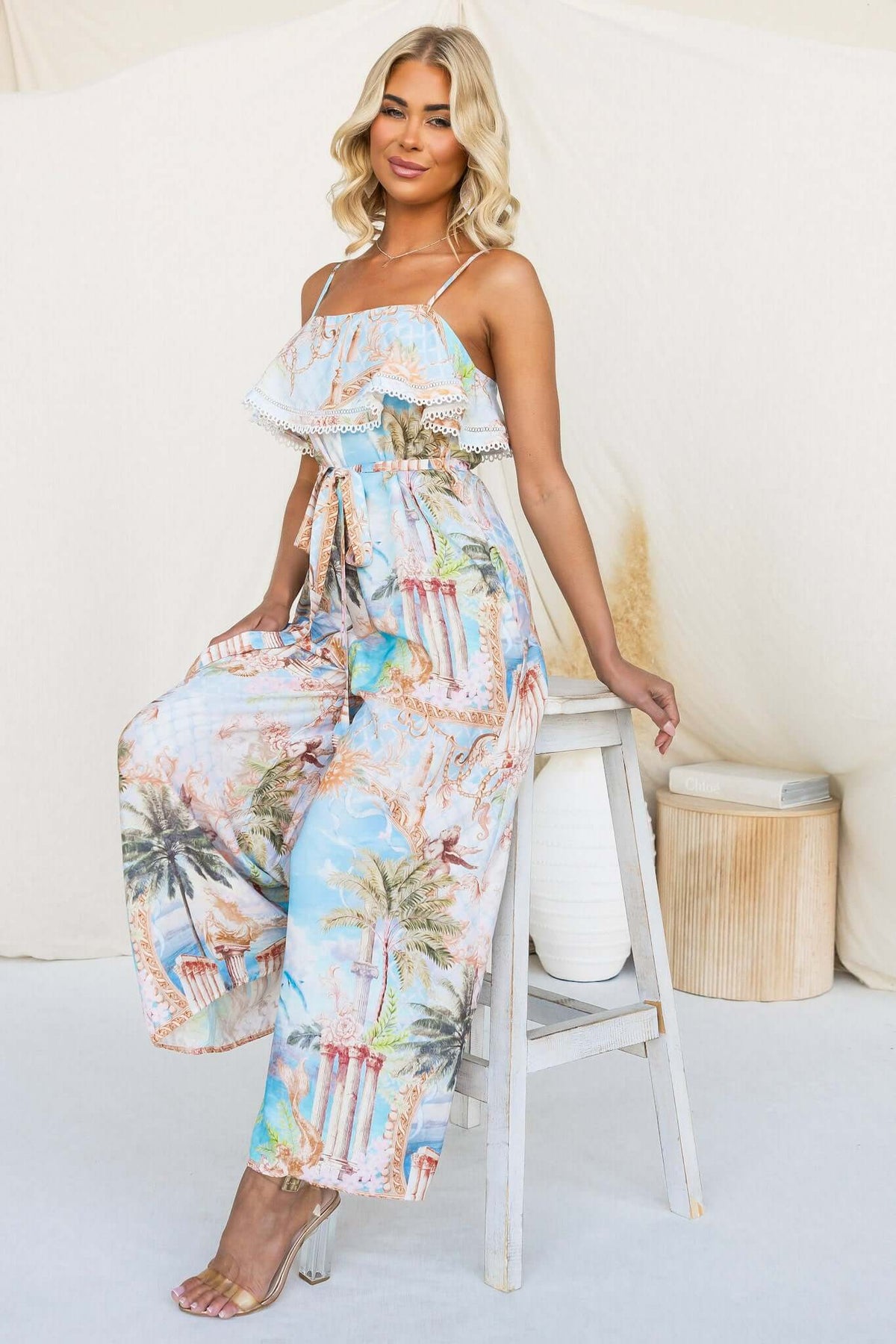 Model wearing Island Escape Jumpsuit with adjustable straps and removable belt, set against a neutral backdrop.