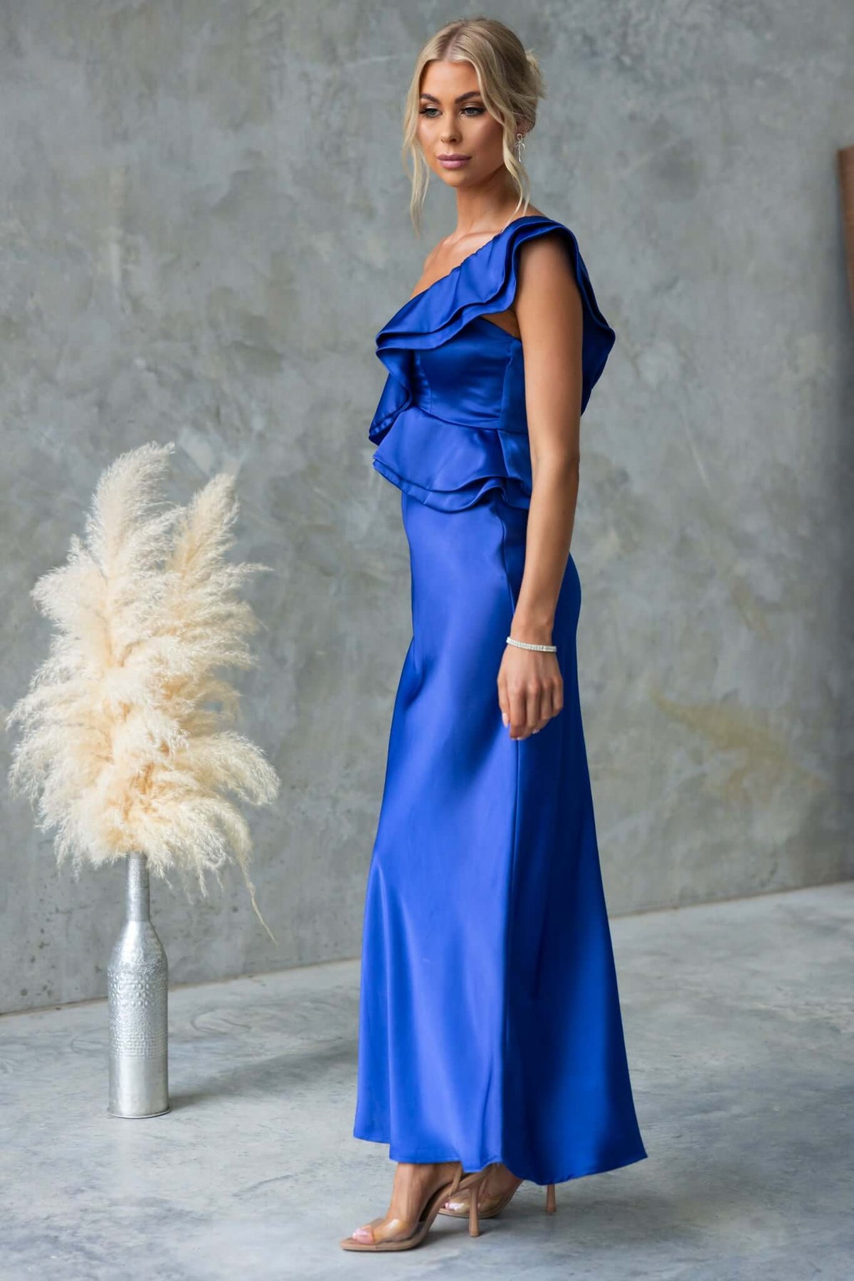 Janiyah Satin Maxi Dress in blue with one-shoulder neckline, styled with heels, featuring padded bust and invisible back zip.