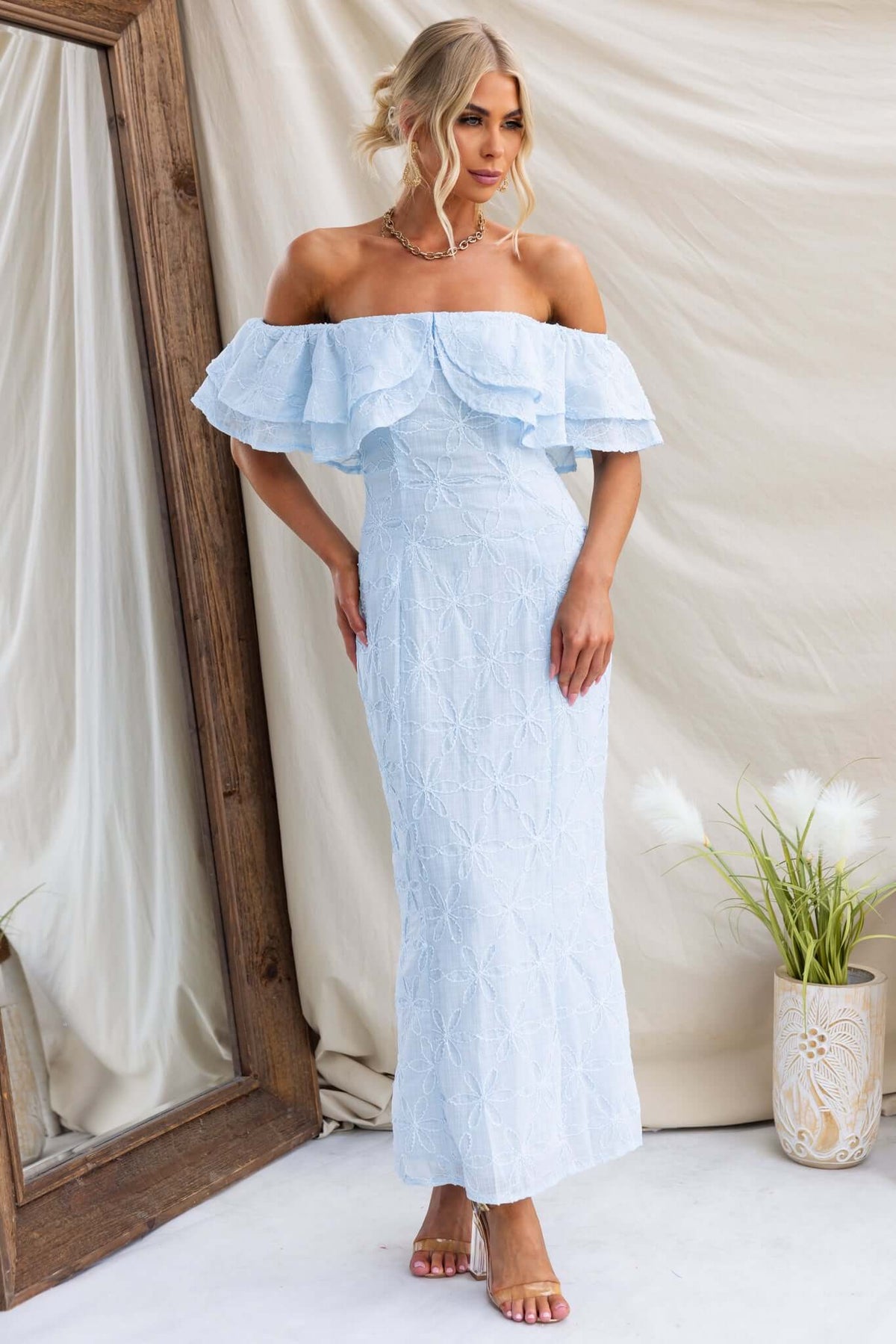 Light blue Jaqcues Maxi Dress with off-shoulder ruffle detail, styled elegantly by a model in a natural setting.