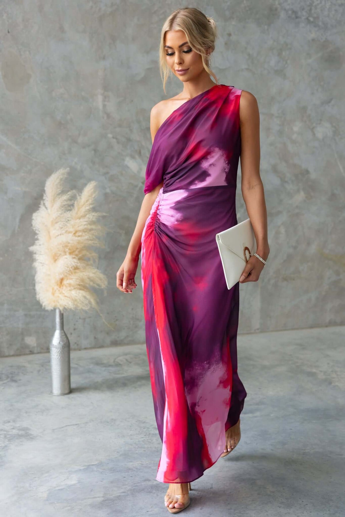 Model wearing Jules Maxi Dress with asymmetric neckline and side ruching, in vibrant purple and pink hues.