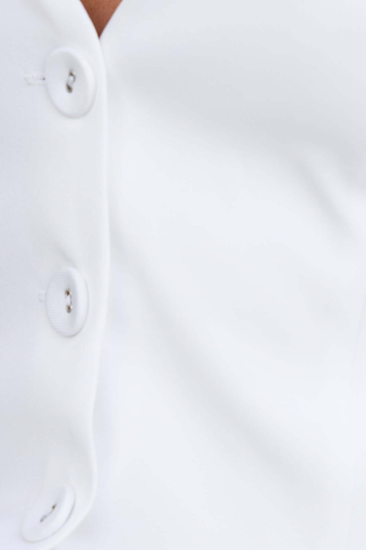 Close-up of white fabric with buttons, showcasing the texture and design details of a stylish garment.