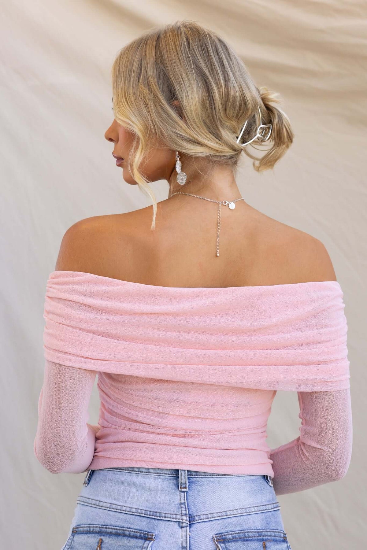 Karmy Top in soft pink with off-shoulder neckline and stretch fabric, styled with high-waisted jeans.