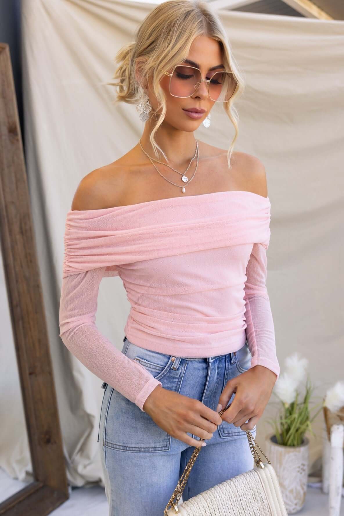 Karmy Top in soft pink, off-shoulder neckline, stretchy material, styled with casual jeans and sunglasses.