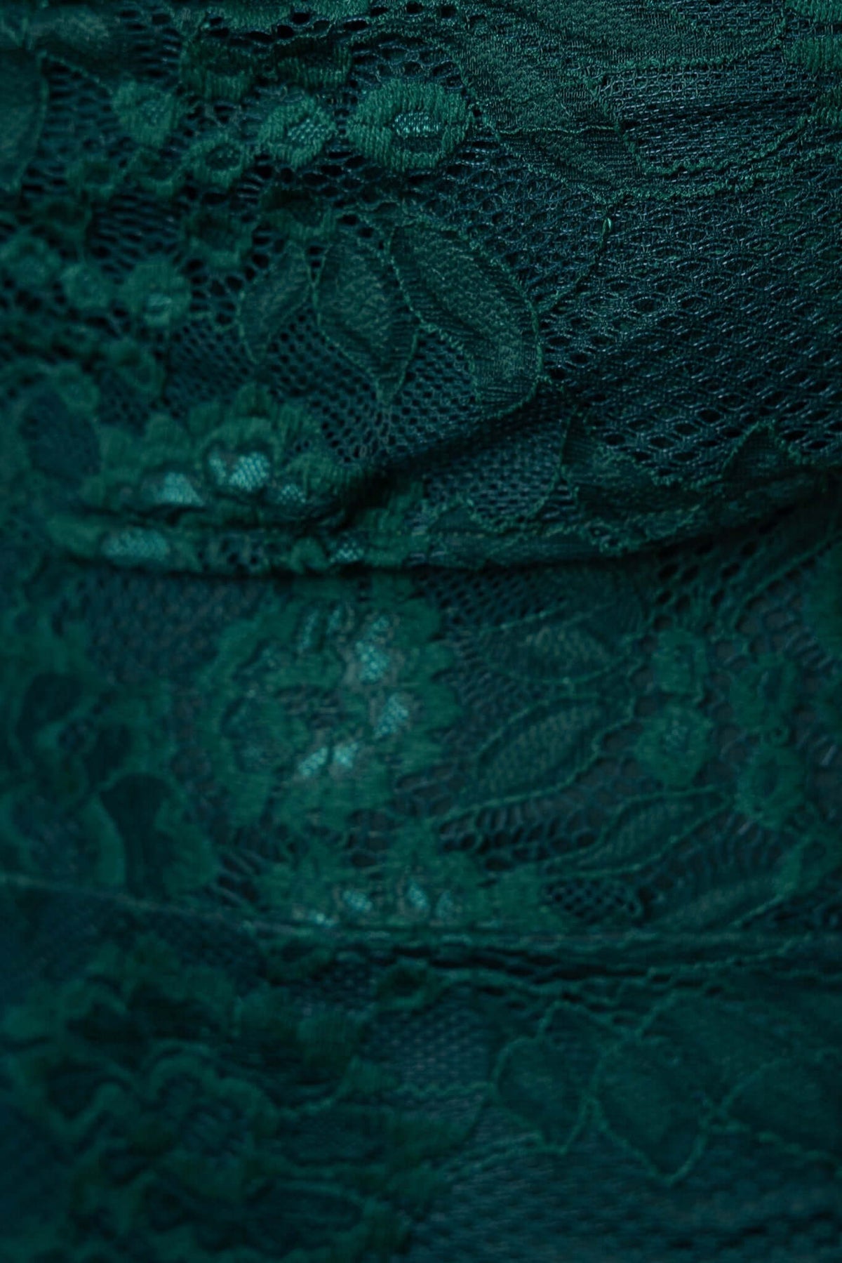 Close-up of dark green lace fabric, showcasing intricate floral patterns and a textured design for the Kearney Midi Dress.