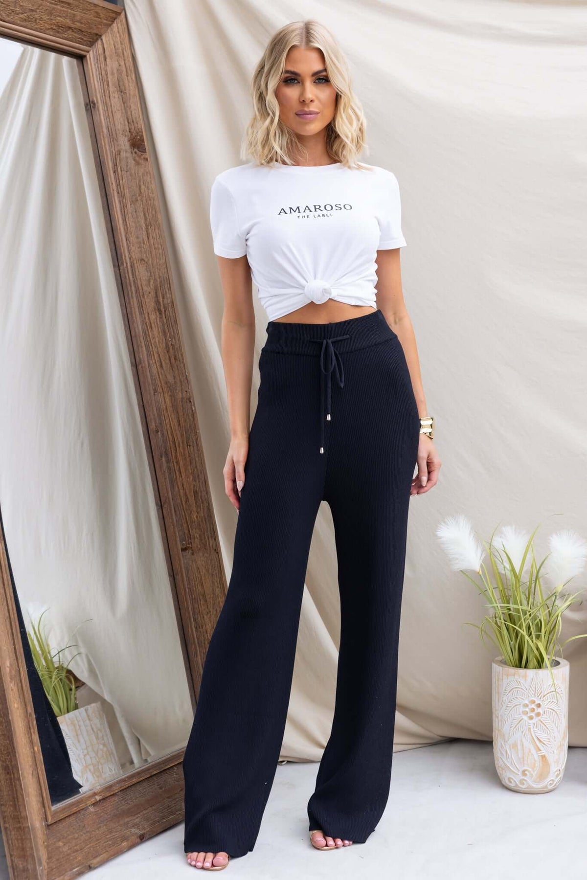 Model wearing Keene Pants in black with a mid-high waist and elastic waistband, styled with a white printed tee.