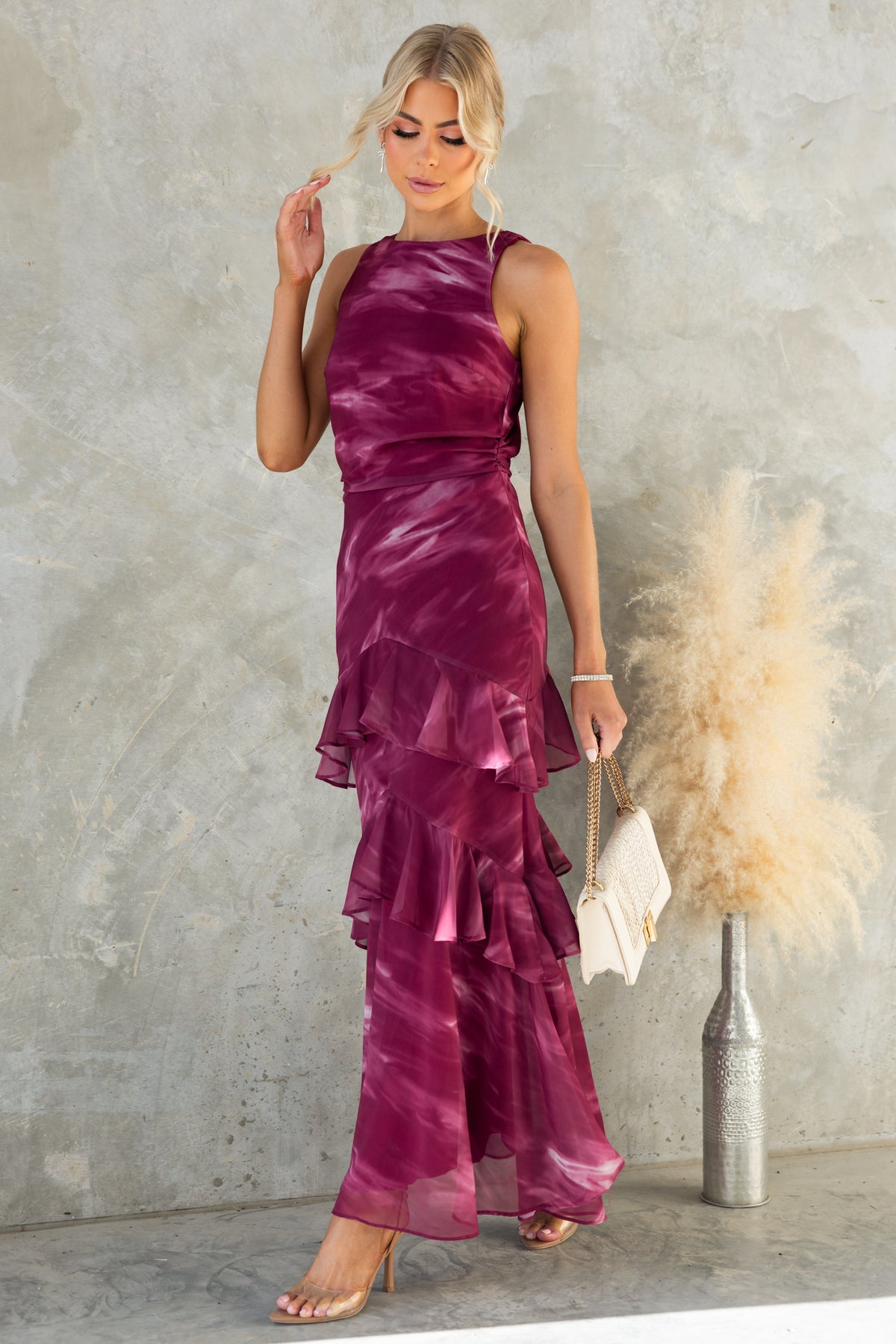 Elegant Kilian Maxi Dress in burgundy with ruffles, high neckline, and fitted silhouette, styled with a chic handbag.