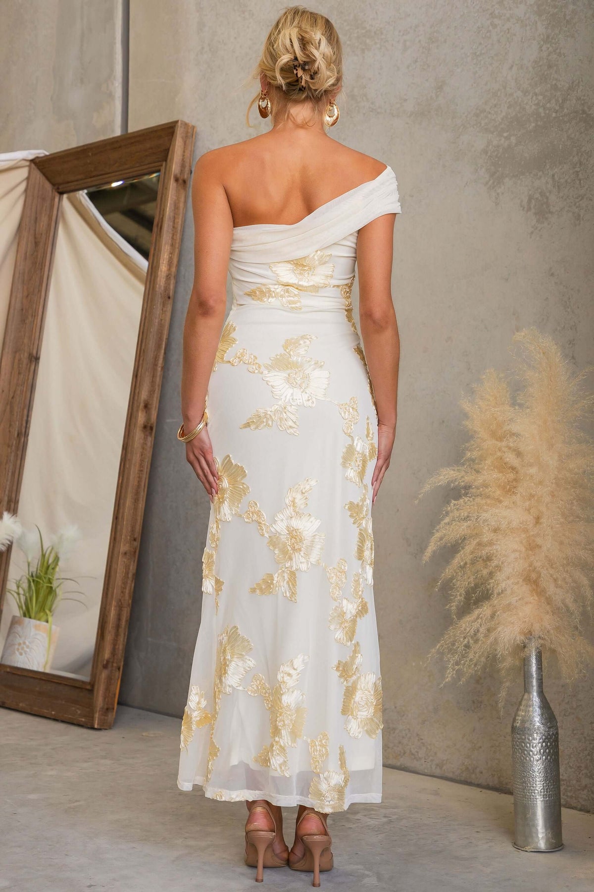 Woman wearing Korren Maxi Dress with one-shoulder neckline, embroidered mesh, showing back view in stylish setting.