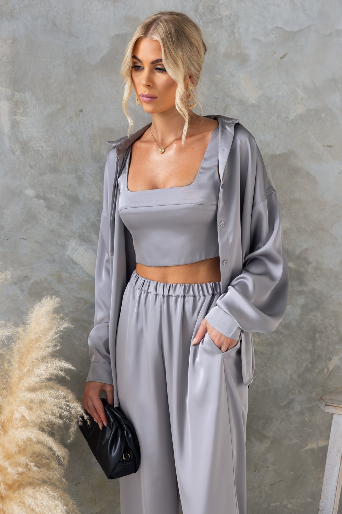 Model wearing a satin Kortez Shirt with a relaxed fit, featuring a button-up front and stylish gray color against a textured backdrop.