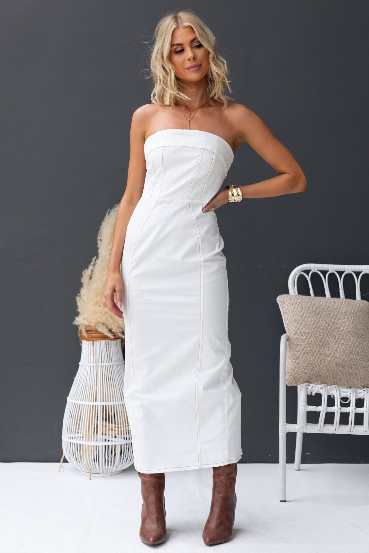 Strapless white denim maxi dress with a fitted design, split at the back, worn with stylish brown ankle boots.