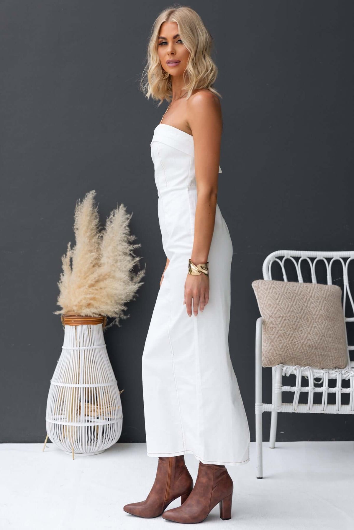 Model showcasing a strapless white denim maxi dress with a back zip and split, styled with brown boots.