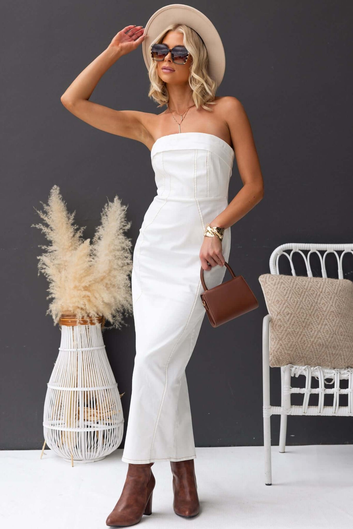 Model wearing a stylish strapless white denim maxi dress with a split back, paired with accessories and boots.