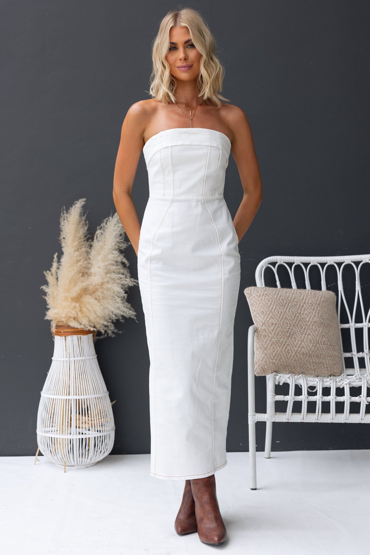 Model wearing a strapless white denim maxi dress with a zip back and split, styled with brown boots.