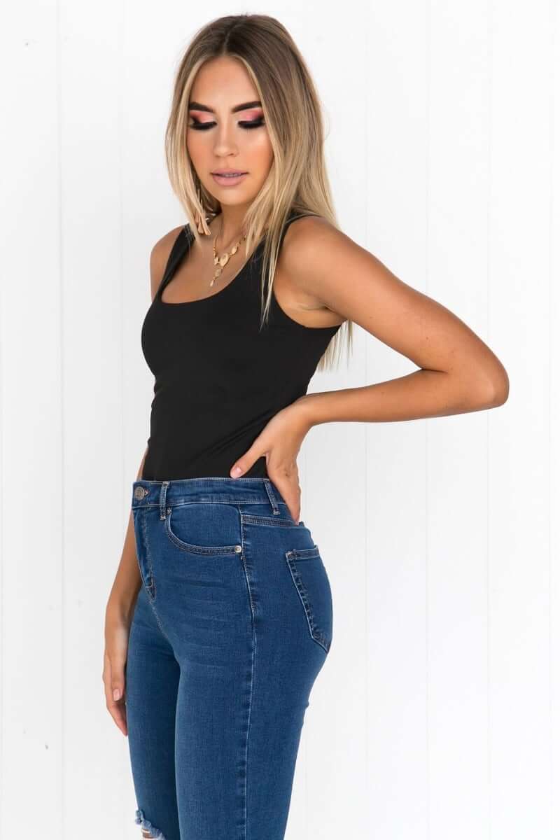 Model wearing Layla Top in black, featuring wide scoop neckline and fitted style, paired with blue jeans.