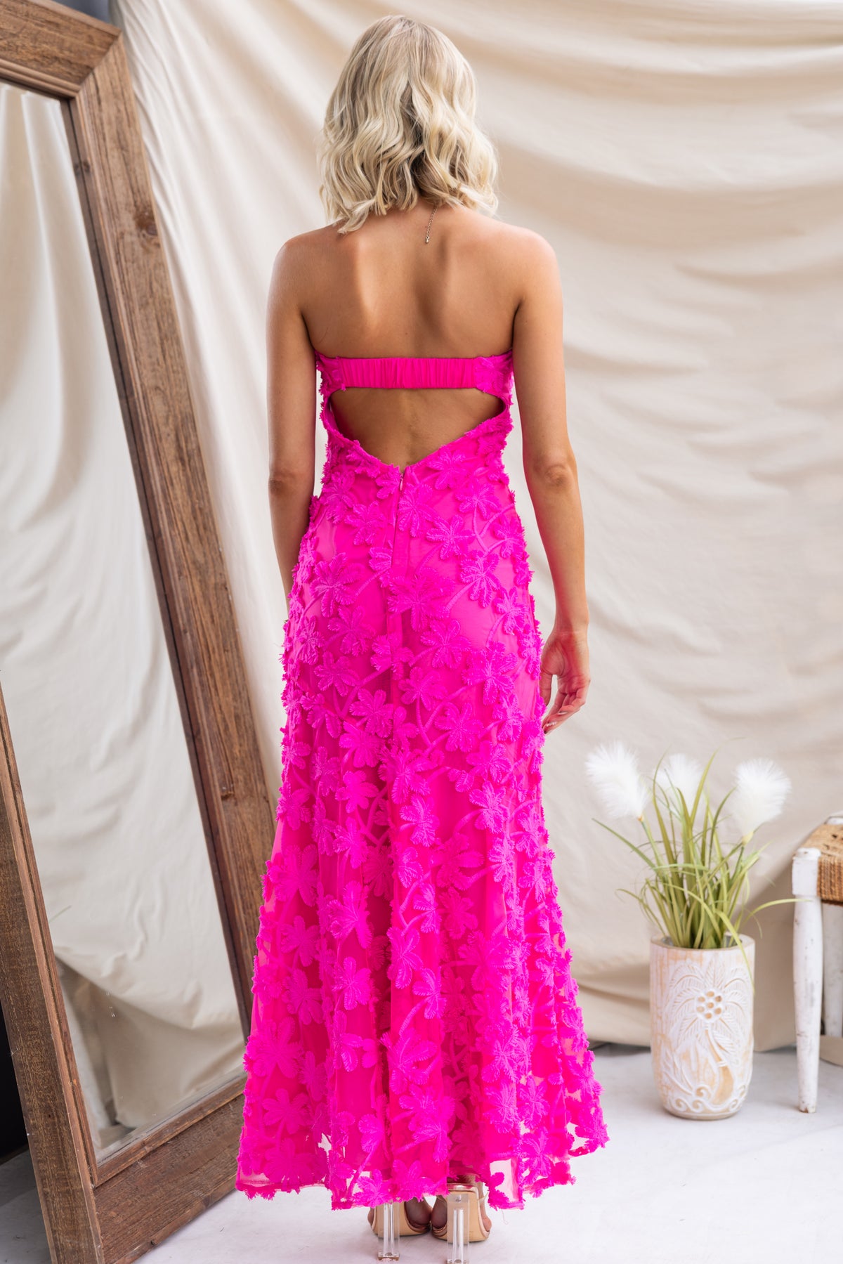 Back view of a model in a hot pink Lilium Maxi Dress with embroidered material and strapless design.