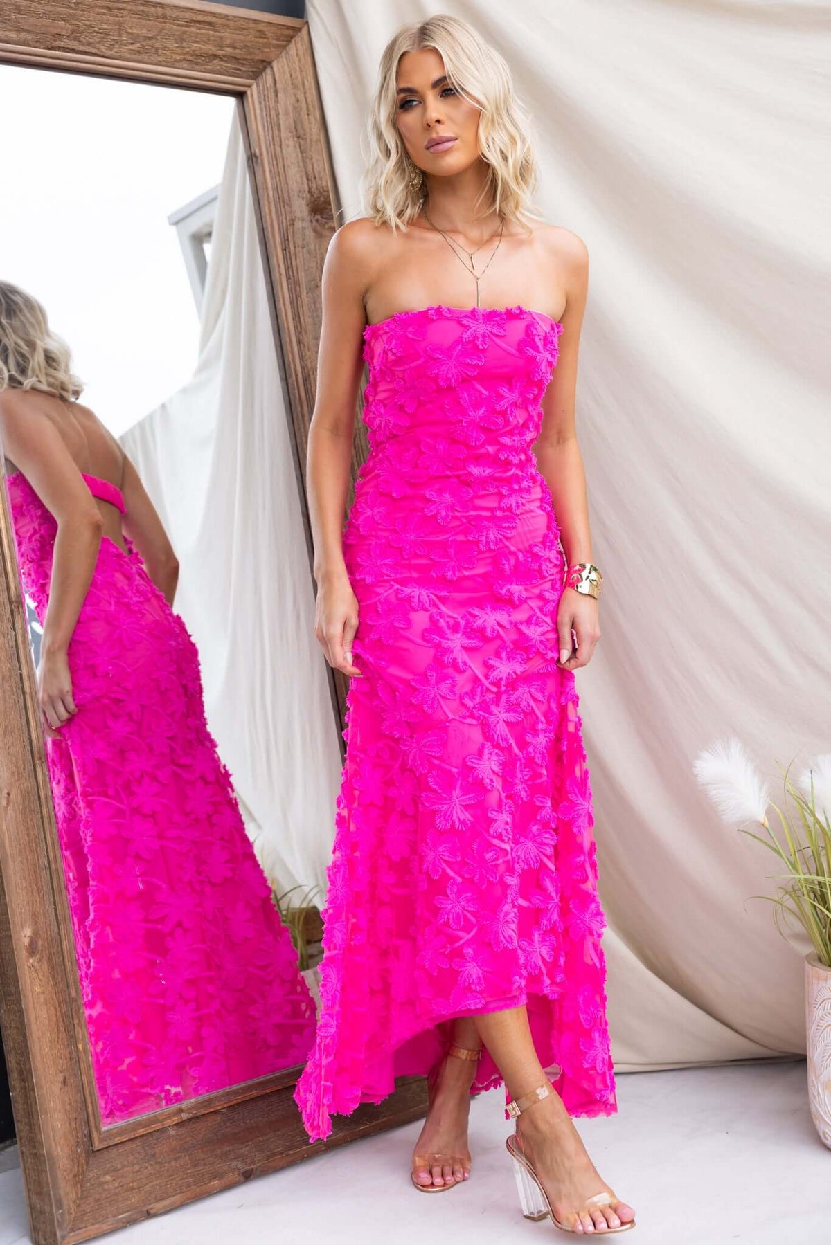 Model wearing a vibrant pink Lilium Maxi Dress, showcasing embroidered material and a strapless design in front of a mirror.