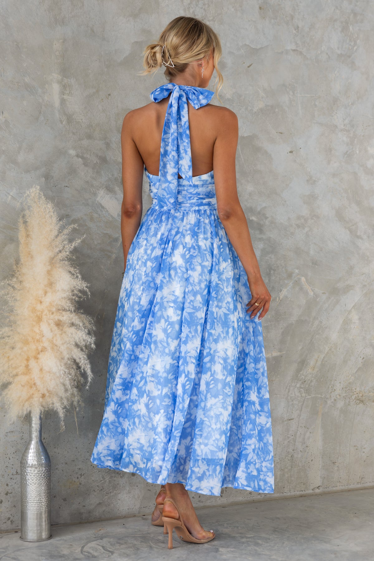 Model wearing the Little Things Maxi Dress with a high tie neckline and floral blue pattern, showcasing the back view.