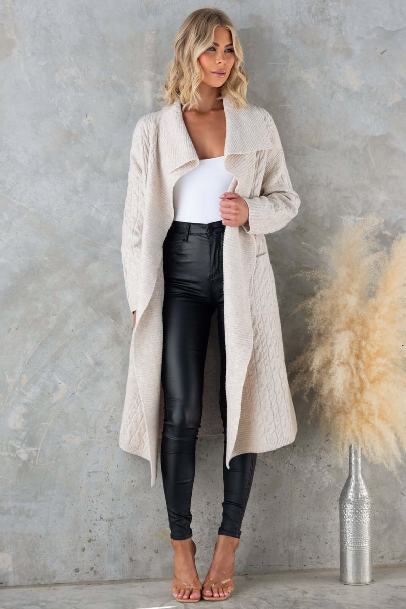 Lyncher Cardigan in cream, featuring a relaxed fit, pockets, and a stylish collar, paired with sleek black pants.