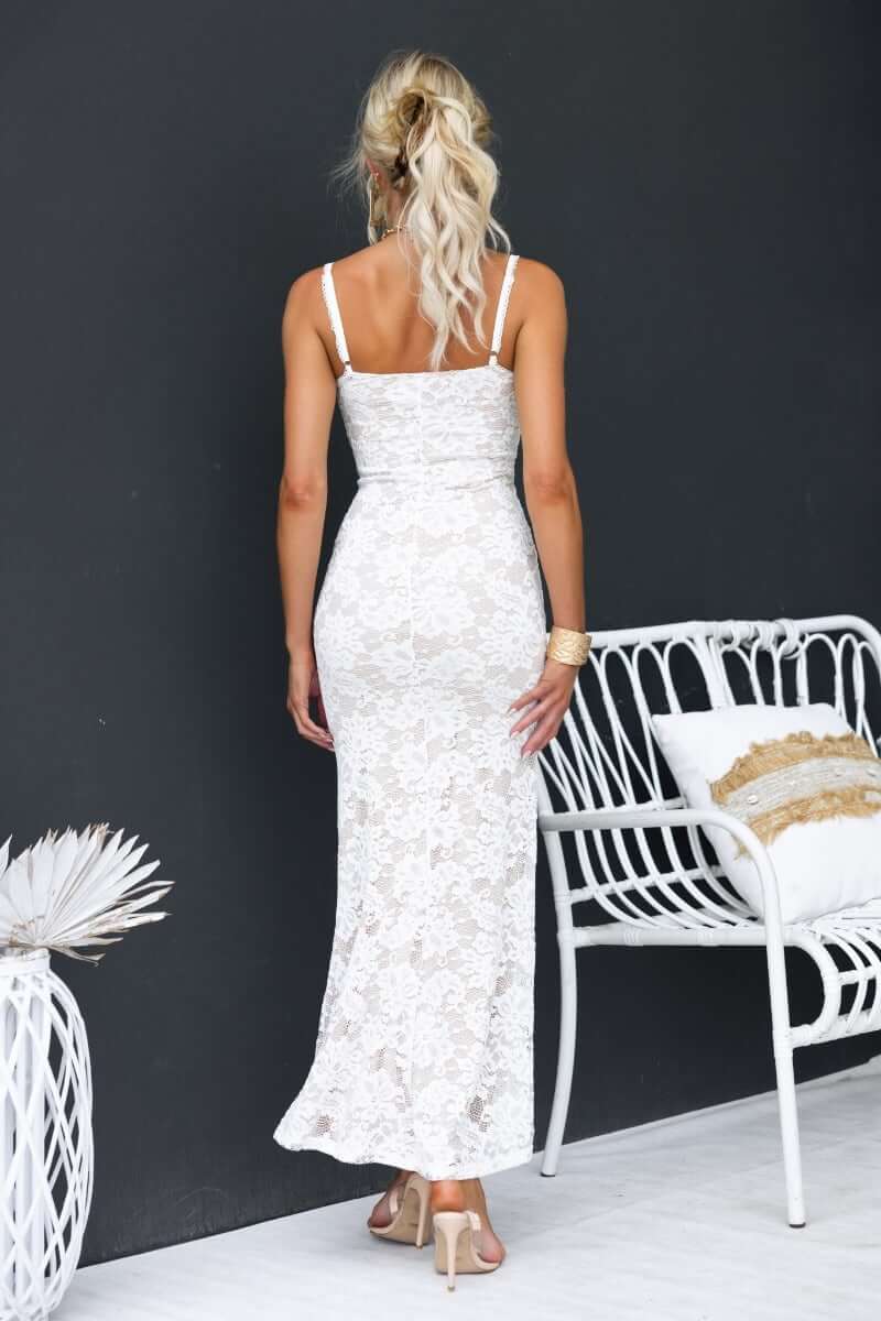 Back view of a woman in a white lace maxi dress with adjustable straps, styled elegantly against a dark background.