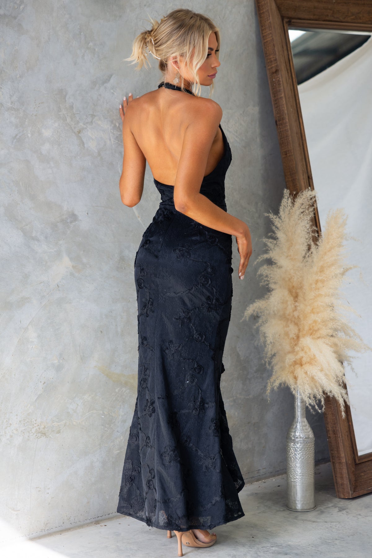 Back view of Metrick Maxi Dress by Amaroso Bridal, featuring a halter neckline and fishtail hem in textured black material.