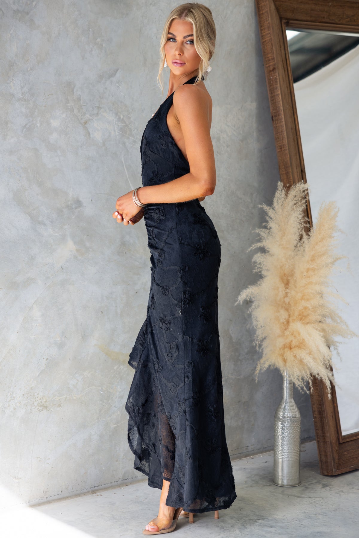 Model showcasing the Metrick Maxi Dress by Amaroso Bridal, featuring a halter neckline and fishtail hem in elegant black.