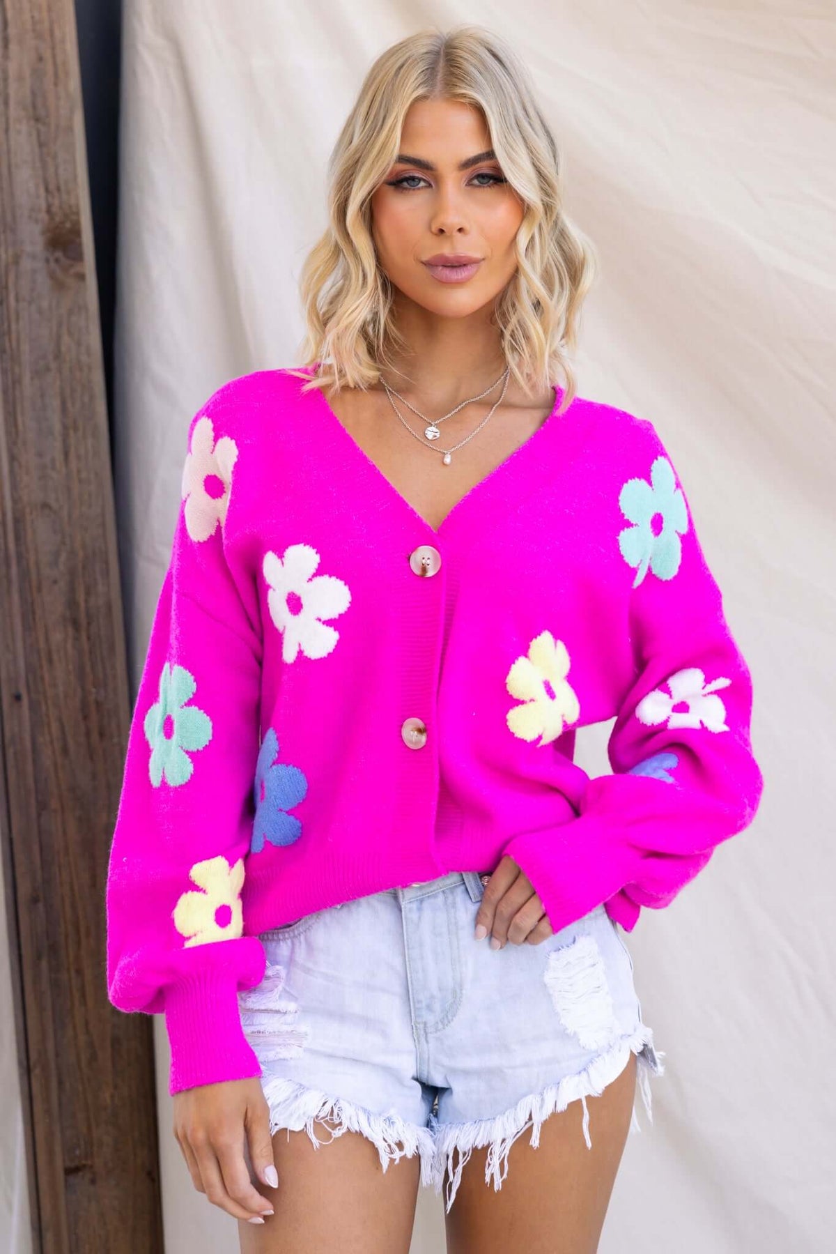 Bright pink Mimsie cardigan with flower patterns, V-neckline, and button-up front, styled with shorts.