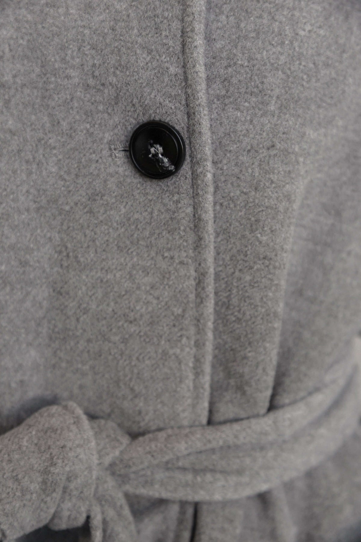 Close-up of Modern Love Coat featuring button closure and removable belt in grey fabric.