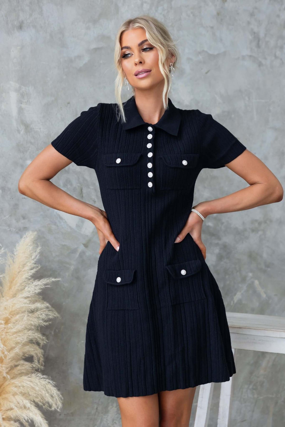 Niall Dress in black with a collar, buttons, and front pockets, made from stretch knit material, modeled by a woman.