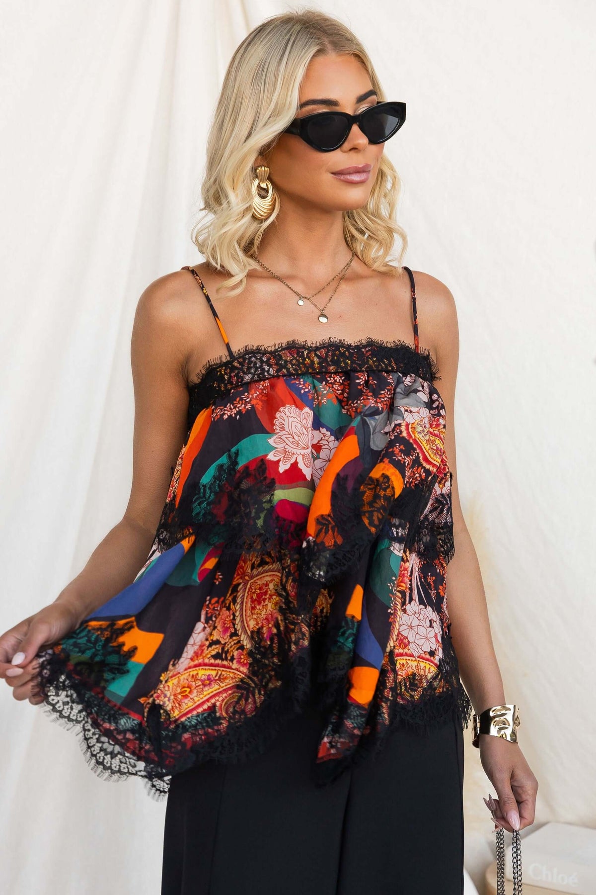 Model wearing a vibrant Nightingale Top with lace detail and adjustable straps, styled with sunglasses and jewelry.