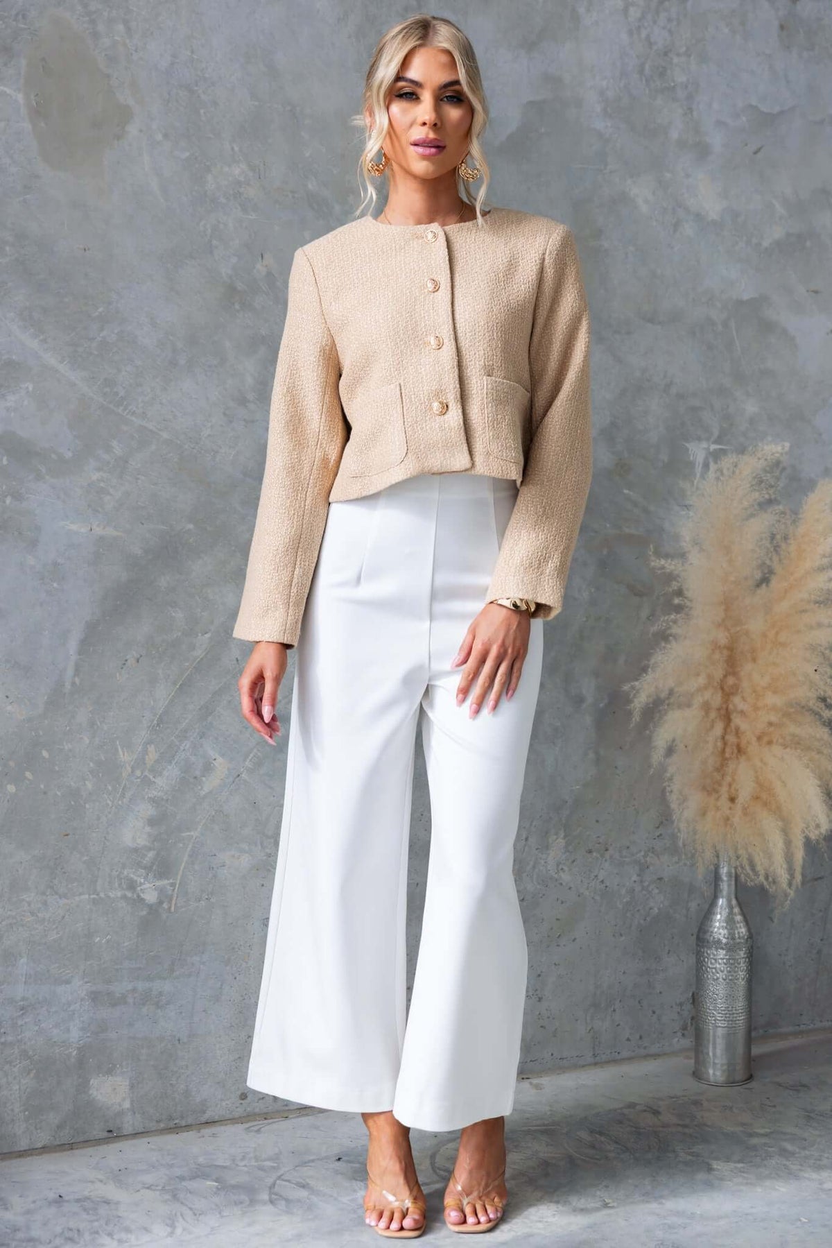 Model wearing the Noelle Jacket in beige with button-up front, paired with white pants, showcasing stylish shoulder pads and pockets.