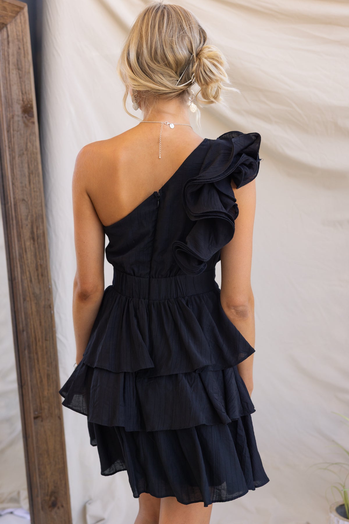 Back view of Orsini Dress featuring one-shoulder design, ruffled strap, and layered skirt in black.