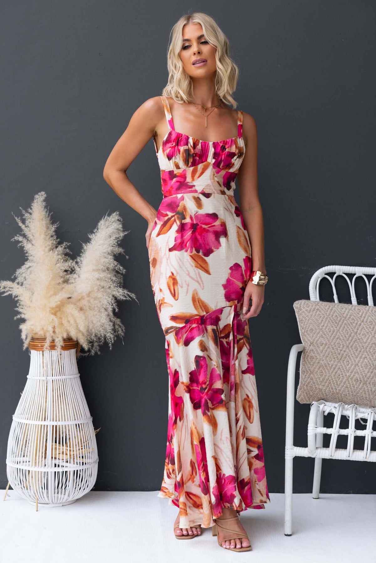 Woman in Ozias Maxi Dress with floral print, adjustable straps, and a front split, styled in a chic setting.