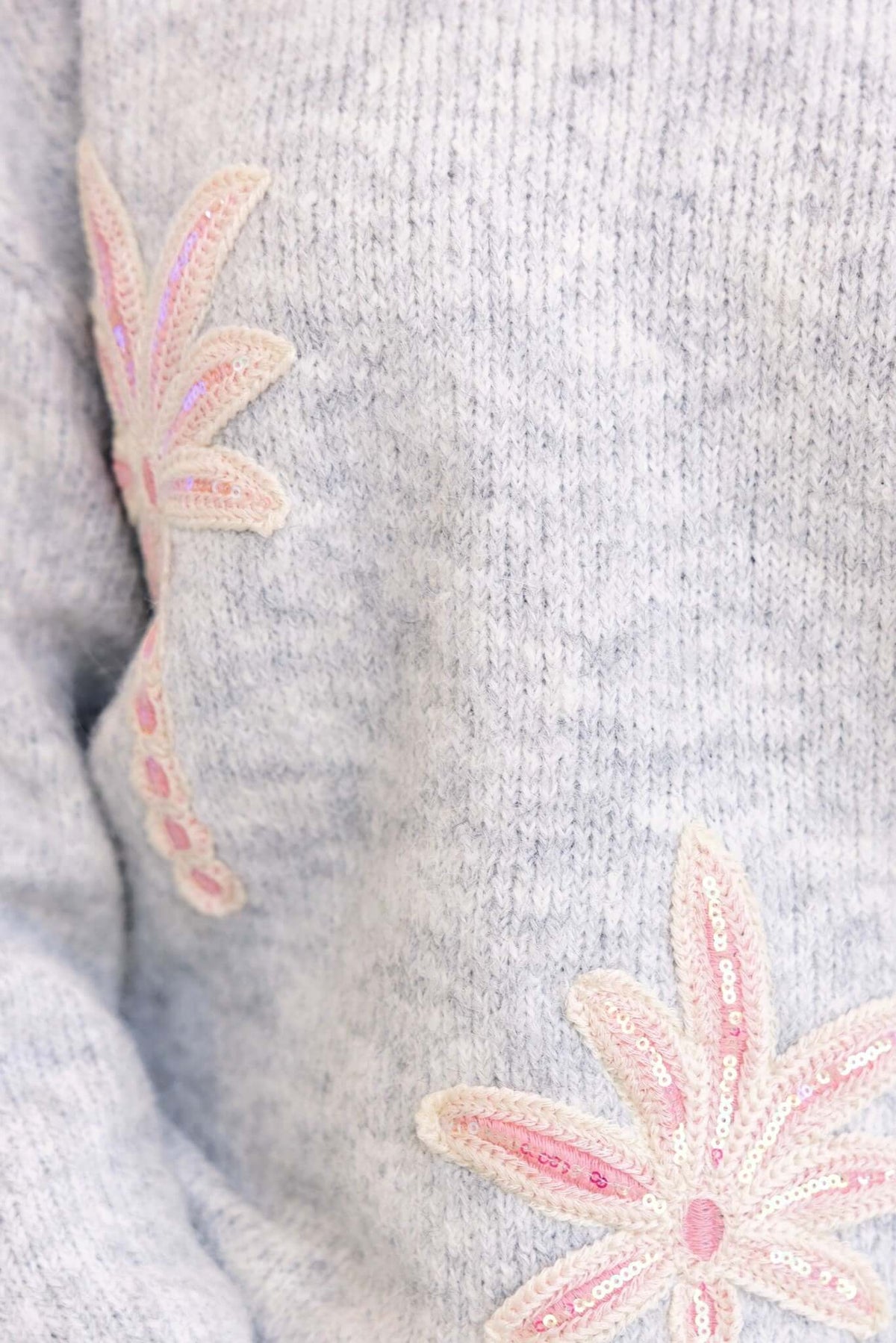 Close-up of the Palmyra Jumper featuring embroidered pink floral details on a soft gray knit background.
