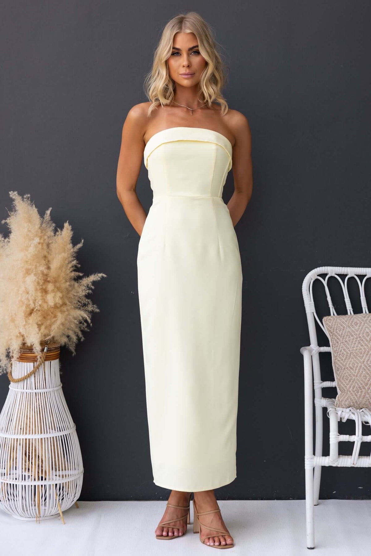Model wearing a strapless Pavlos Maxi Dress in yellow, showcasing its boning, back split, and elegant design.
