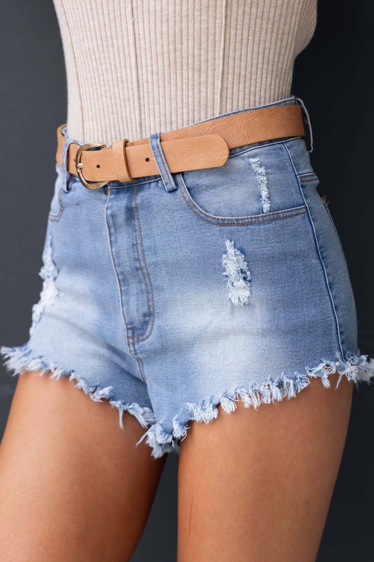 High-waisted distressed denim shorts with raw hemline and pockets, styled with a belt.